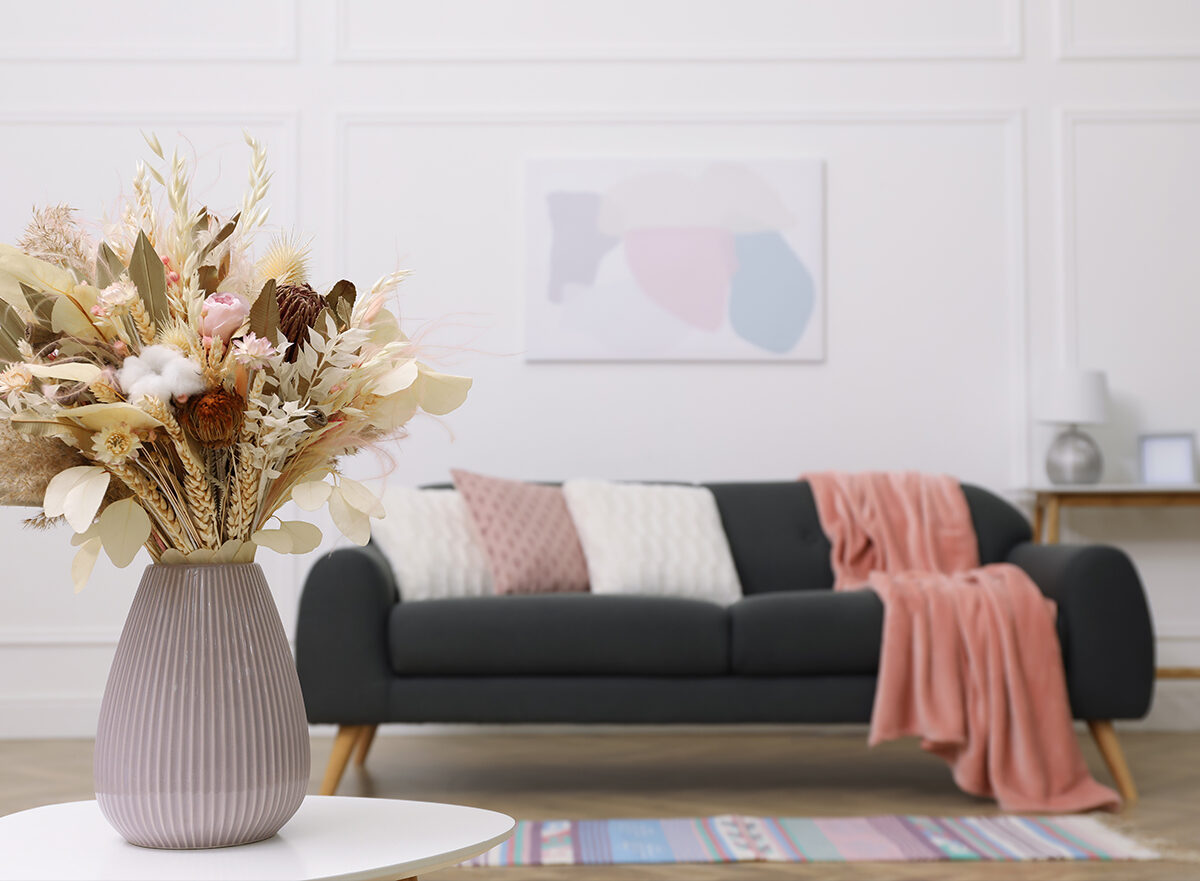 Beautiful sofa with cushions and a dried flower bouquet in a warm living room