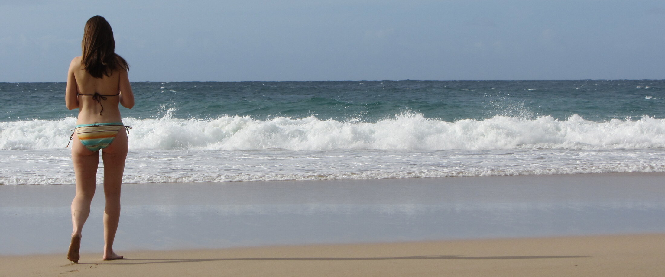 Woman standing at the edge of the ocean, looking out at the waves